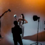 In a photo studio the posing for a photo and the guy clicking a picture of her and rest is helping for perfect shot