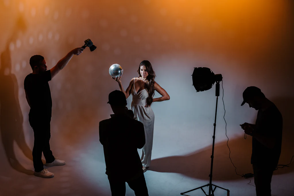 In a photo studio the posing for a photo and the guy clicking a picture of her and rest is helping for perfect shot